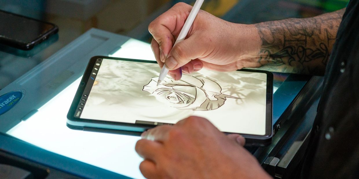 A person with a right arm tattoo holding an electronic tablet and doing a digital illustration