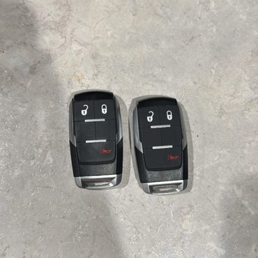 Two black car key fobs with lock, unlock, and alarm buttons on a light gray surface.