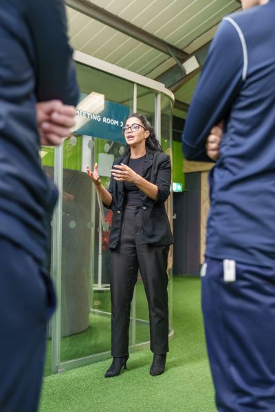 Woman in black suit speaking to two people outside a meeting room.