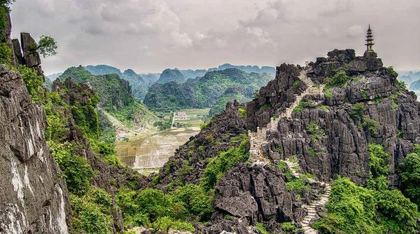 Rocky mountain path with stone stairs and pagoda overlooking green valley.