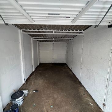 Empty garage space with white walls and a brown floor.