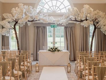 Wedding ceremony styling with sage green chair sashes gold lanterns and white blossom trees
