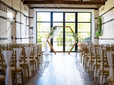 Wedding ceremony styling at Lillibrooke Manor with chair drapes and a hexagon archway & petals
