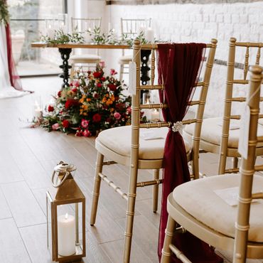 Burhundy themed wedding ceremony styling featuring chair sashes lanterns and flowers.