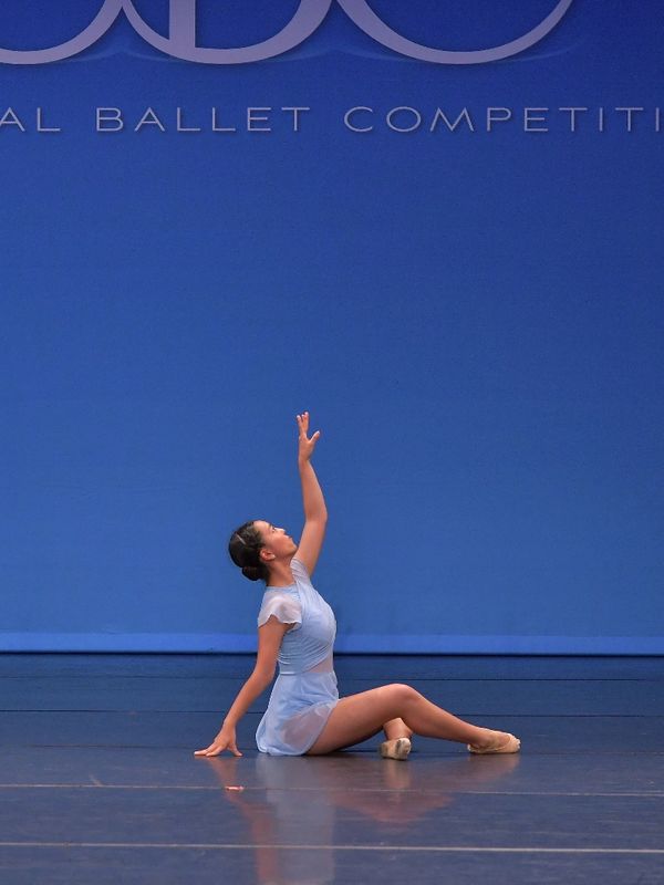 Ballet dancer in blue costume performing on stage with arm raised.