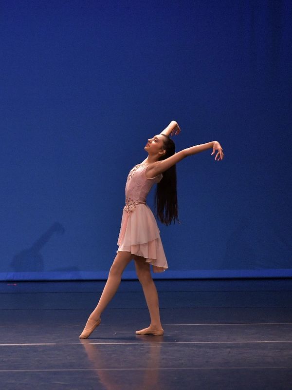 A ballerina gracefully poses on stage in a pink dress against a blue backdrop.
