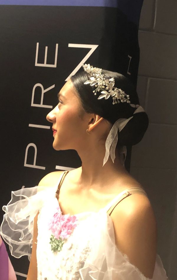 Young woman in a white dress with floral headpiece looking to the side.