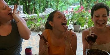 3 women laughing and licking chocolate off their fingers outside in the Costa Rican jungle