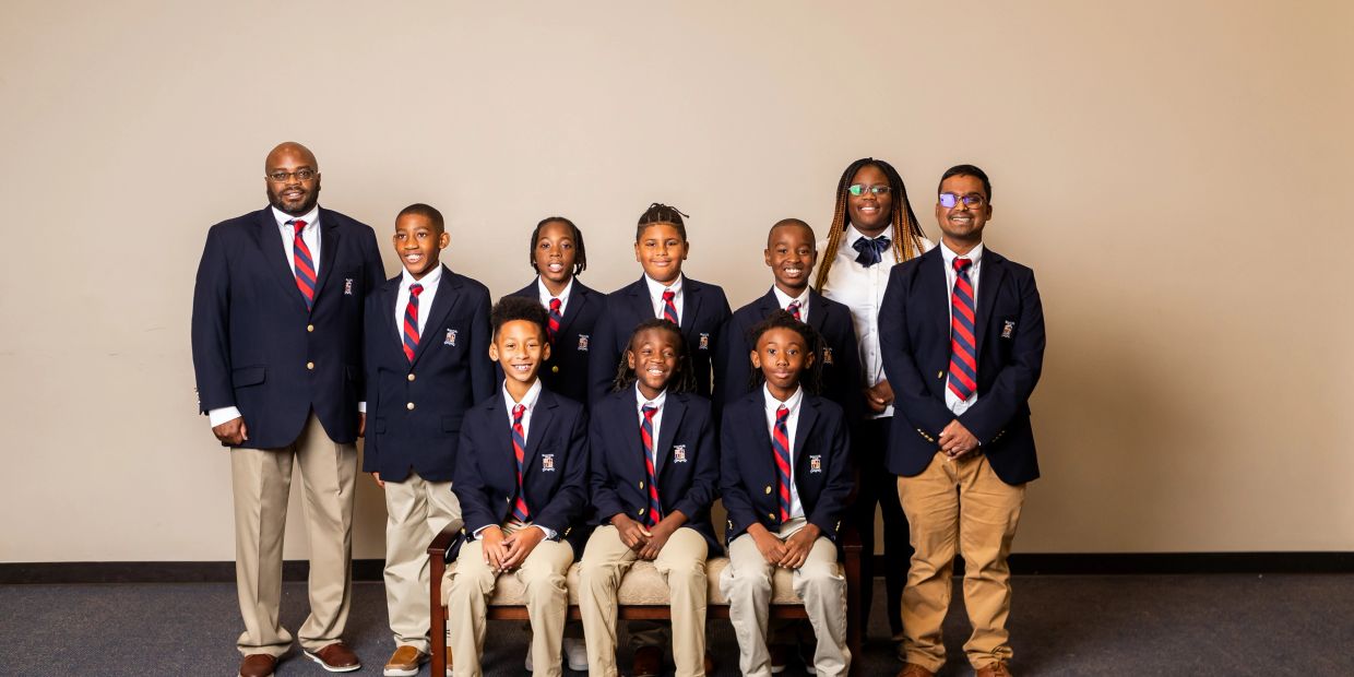 Group photo of students and two adults in formal attire against a plain wall.