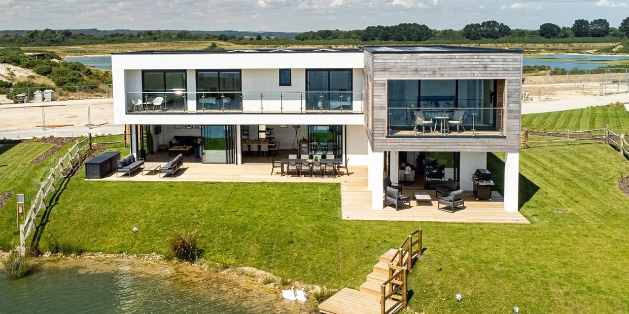 Modern two-story house with large windows and a lakeside view.