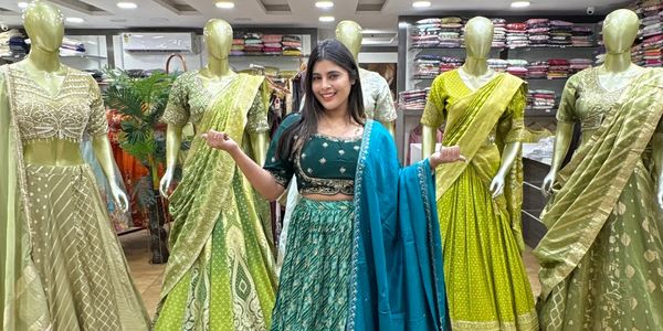 Woman in a teal traditional outfit stands among mannequins dressed in green ethnic wear.