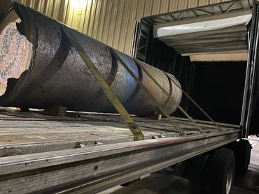 Large cylindrical metal object secured inside a truck trailer with straps.