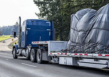 A blue semi-truck hauling a covered load on a highway.