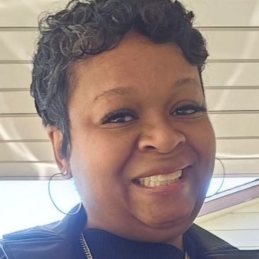 A woman smiling outdoors with hoop earrings.
