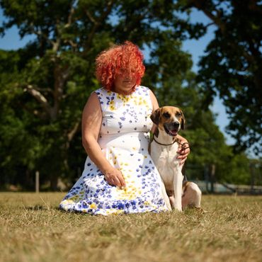 Woman with red curly hair kneels on grass with a happy dog.
