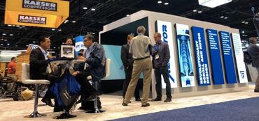 People networking at a Kaeser Compressors booth in a trade show.