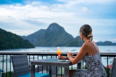 A woman watching the view of the bay and the island while having a drink.