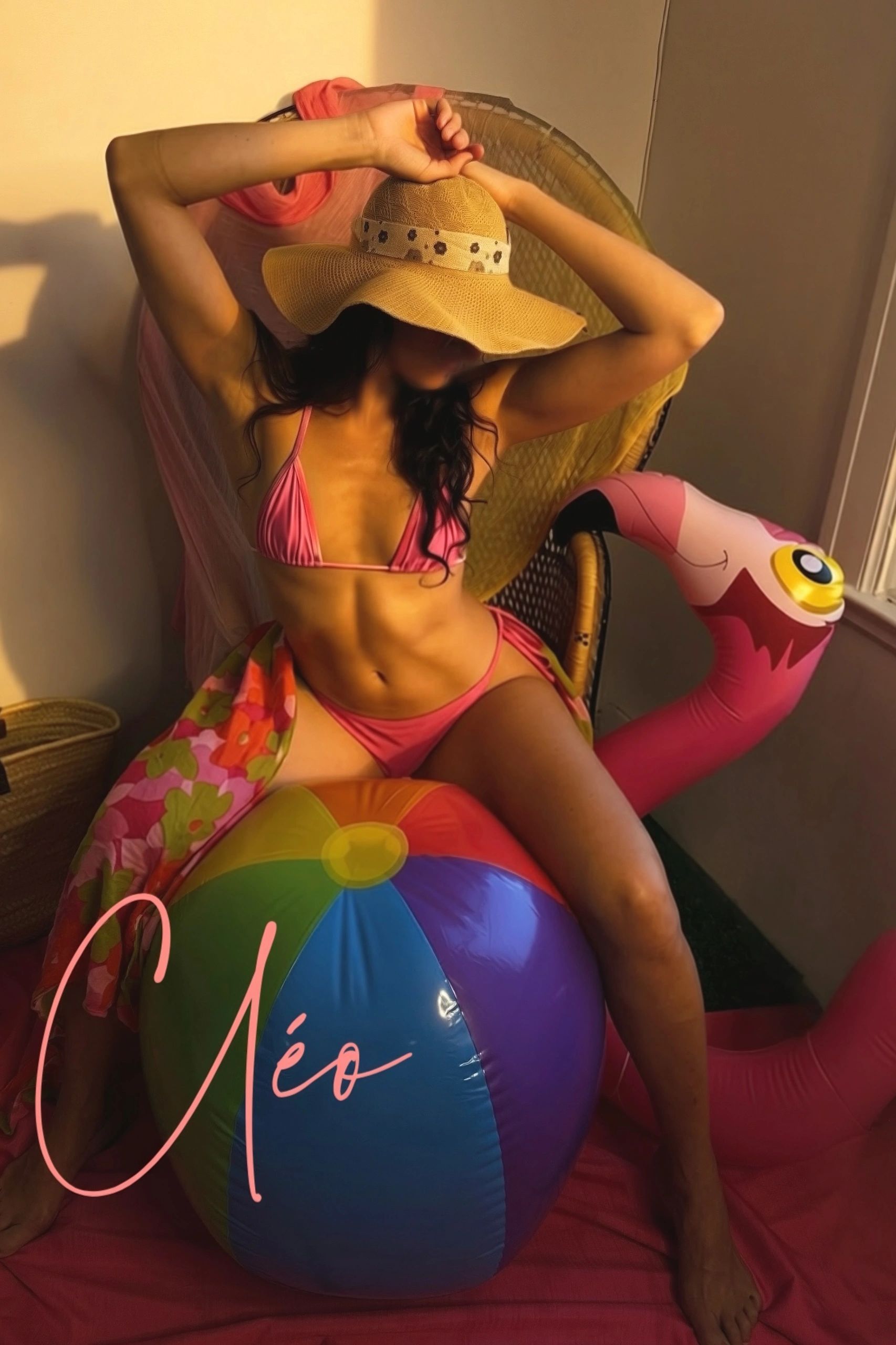 Femme en bikini rose avec chapeau de paille, jouant avec un ballon de plage coloré et une bouée flamant rose.