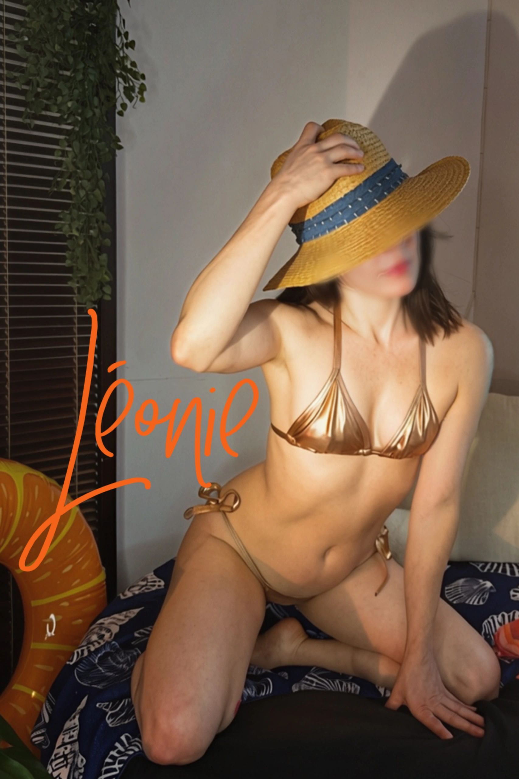 Femme en bikini doré avec chapeau de paille bleue.