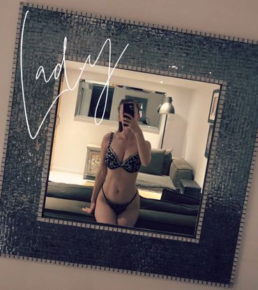 A woman takes a mirror selfie in lingerie inside a cozy living room.