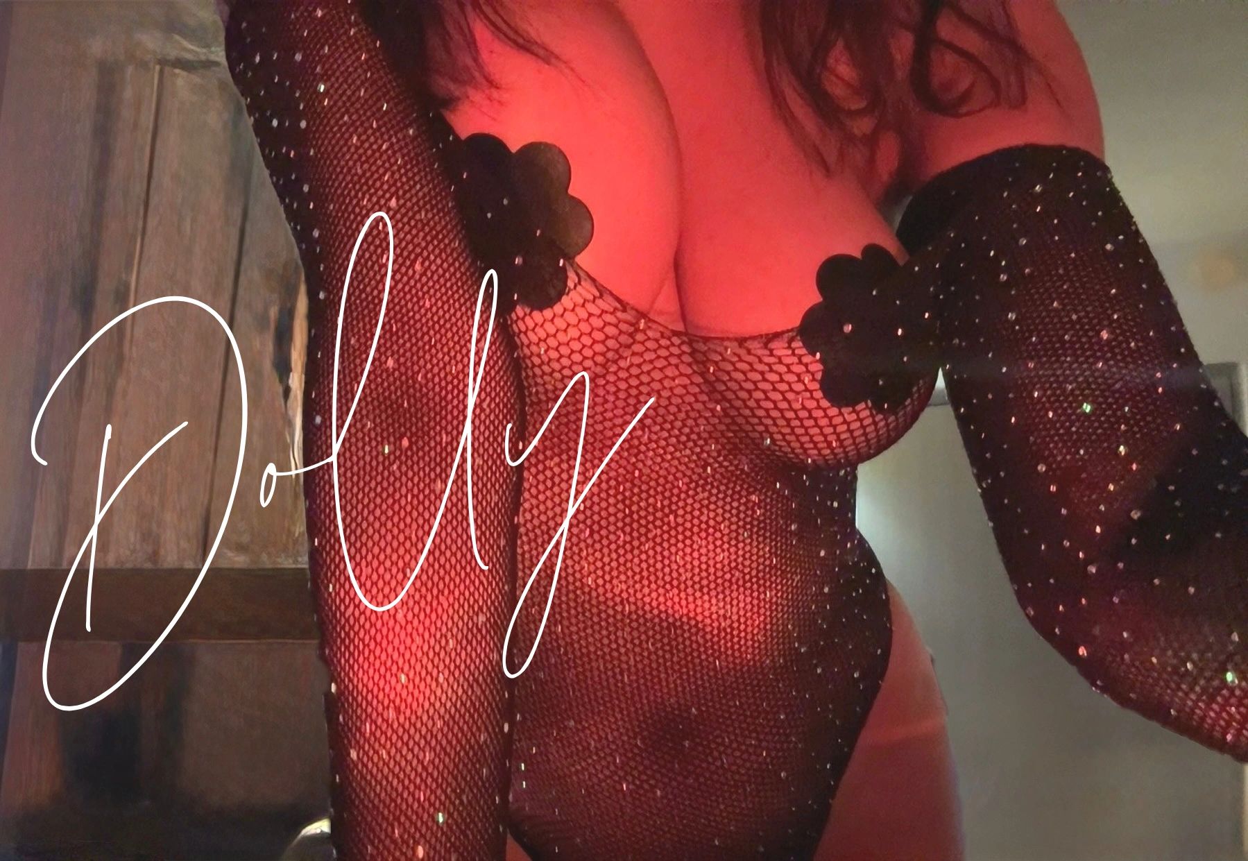 Close-up of a person in a sparkly black fishnet outfit with floral nipple covers, bathed in red light.