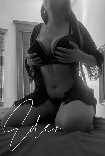 Person in black lingerie posing on a bed with soft lighting.