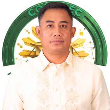 A man in a traditional embroidered shirt stands in front of a green and gold emblem.