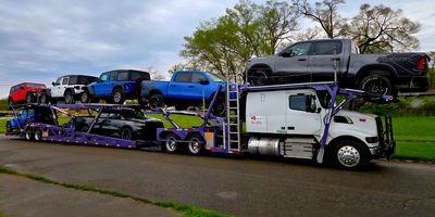 A white semi-truck hauling multiple pickup trucks on a car carrier trailer.