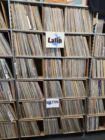 Shelves filled with organized Latin vinyl records in a music store.
