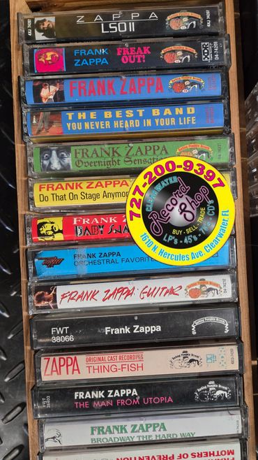 A collection of Frank Zappa cassette tapes in a wooden drawer with a record shop sticker.