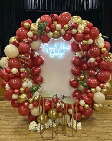Balloon arch with red, gold, and cream colors and a 'Good Vibes Only' neon sign.