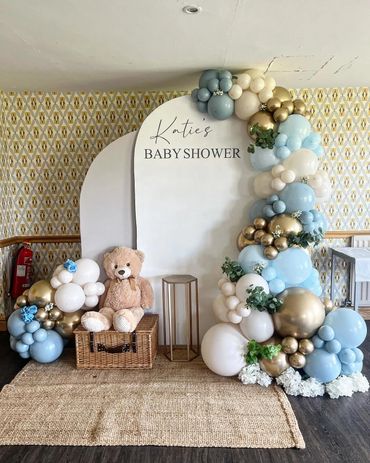 Elegant baby shower setup with balloons, teddy bear, and personalized sign.
