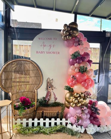 Baby shower setup with balloons, flowers, and a rattan chair.
