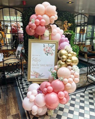 Elegant baby shower setup with pink and gold balloons and floral accents.