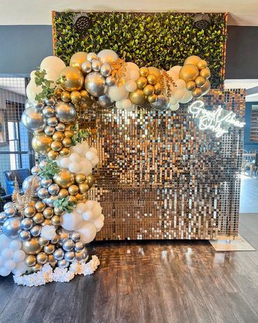 Elegant balloon arch with gold, silver, and white balloons against a shimmering gold backdrop.