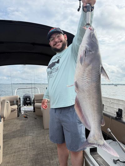 Man proudly holds a large fish on a boat under a cloudy sky.
