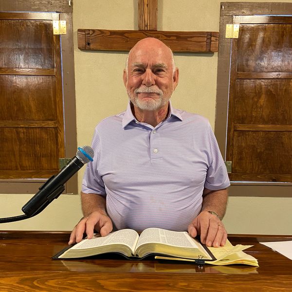 Elderly man with a Bible and microphone in a church setting.