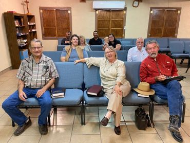 Group of people sitting in a church with Bibles on seats.
