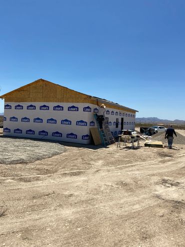 Workers building a house covered with Lowe's branded wrap in a desert area.
