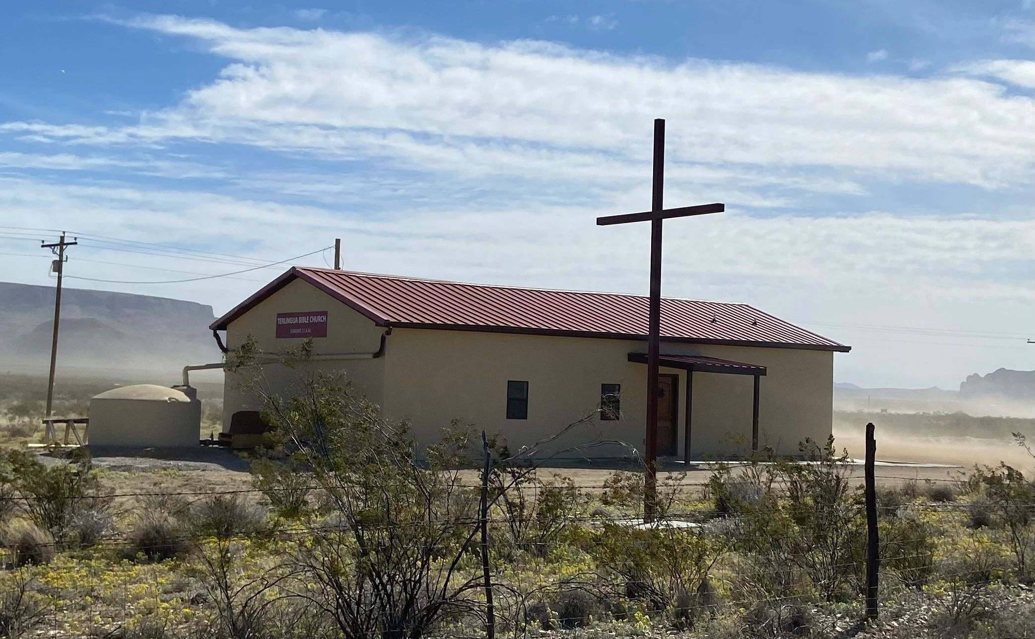 A small church with a red roof and large cross in a desert landscape.