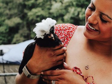 Smiling woman in red dress holding a black and white crested chicken outdoors.