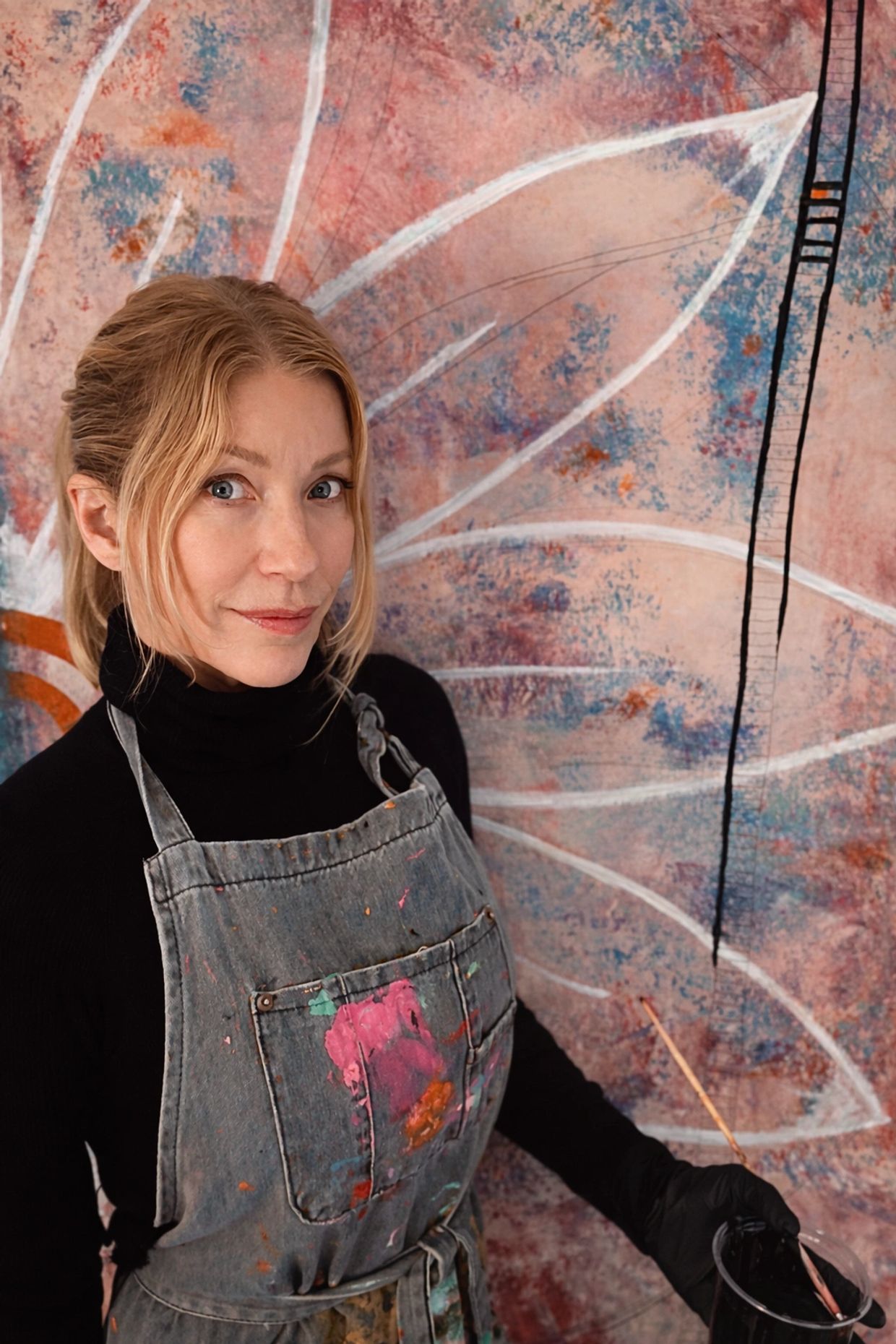 Female artist in apron painting a large abstract mural.