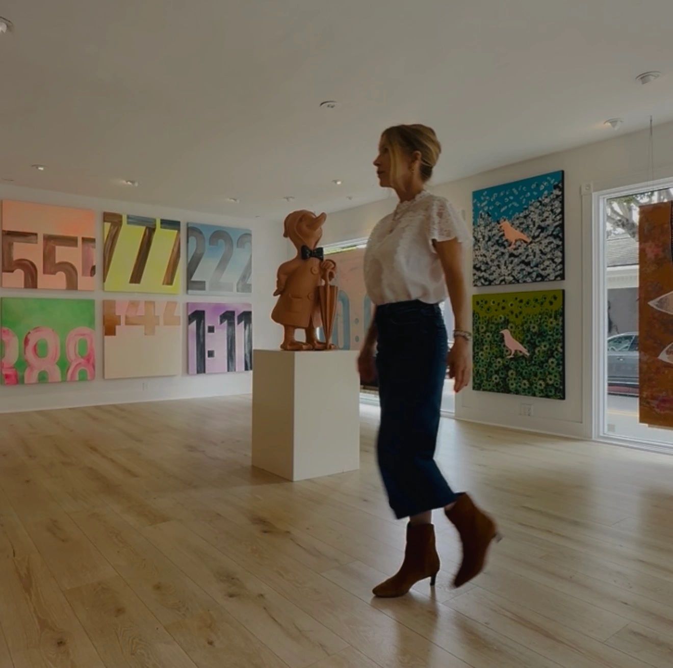 Woman walking in an art gallery with colorful paintings and a duck sculpture.