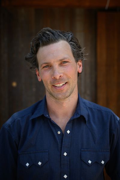Smiling man in a blue shirt with a rustic wooden background.
