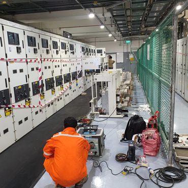 Technician in orange working in an industrial electrical control room.