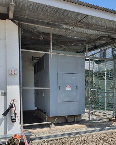Gray high voltage electrical equipment inside fenced area with warning signs.