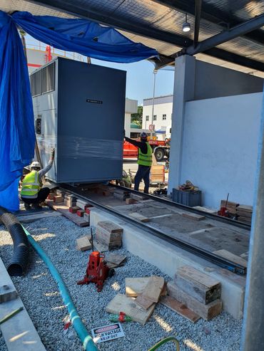 Workers install a large dry transformer on a rail system at an industrial site.