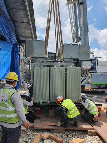 Workers install a large industrial transformer outdoors on a sunny day.