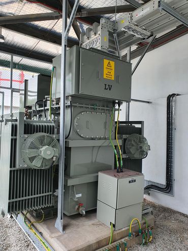 Industrial electrical transformer with safety warning sign and cooling fans.