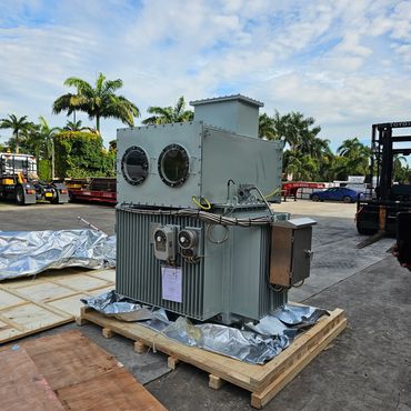 Industrial transformer placed outdoors on a wooden pallet under a blue sky.
